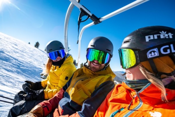 3 skiers sitting on a ski lift talking to each other