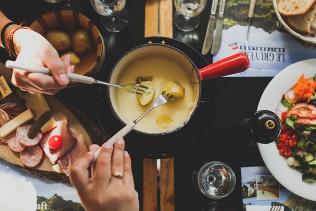 2 people dipping potatoes into a cheese fondue