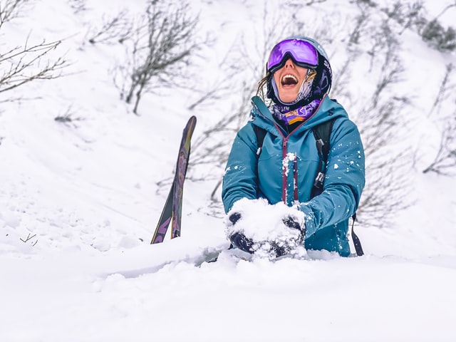 Happy lady dressed in ski wear sitting in the snow in Niseko