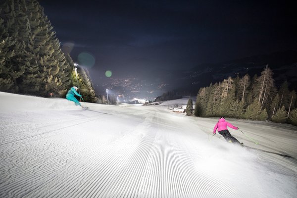 2 skiers skiing down a piste at night in Alpbach