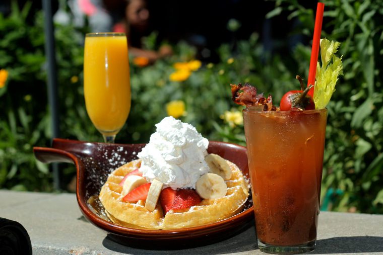 Thick pancake with strawberries and banana, next to a Bloody Mary cocktail and glass of orange juice. 