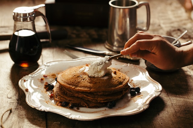 A man spreading cream on top of a stack of buckwheat pancakes