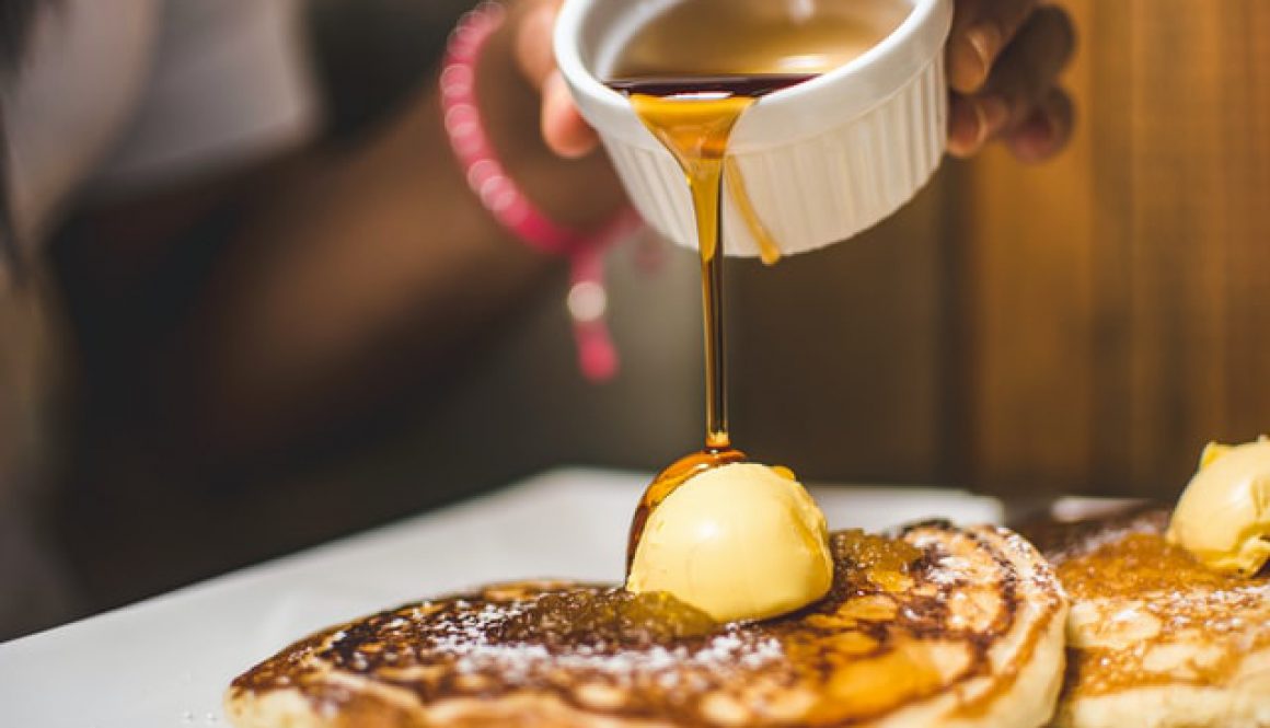 A woman pouring a pot of syrup over pancakes