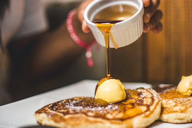 Woman pouring a pot of syrup over pancakes