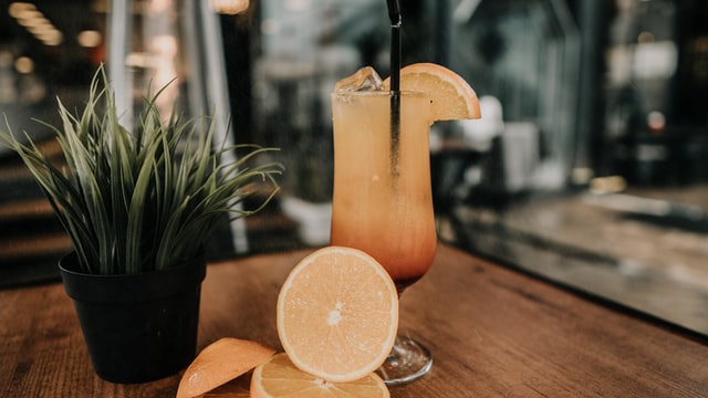 Clear glass of orange drink garnished with a black straw and piece of orange