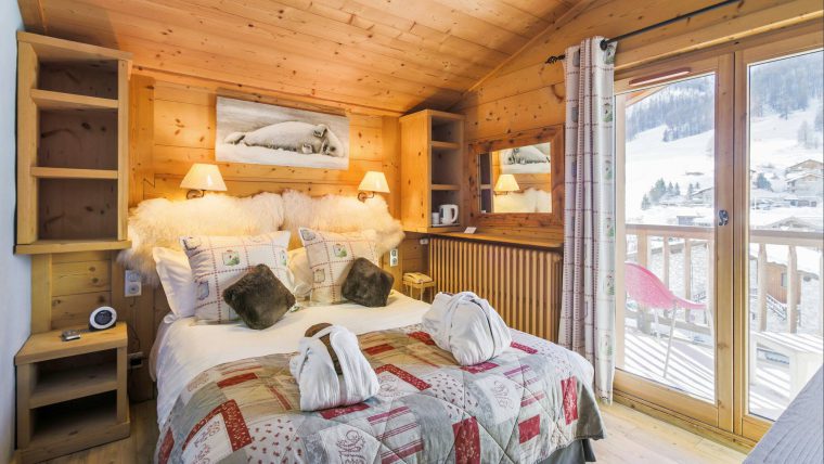 A large cosy bed with in a wooden room with large windows showing a view of the mountains