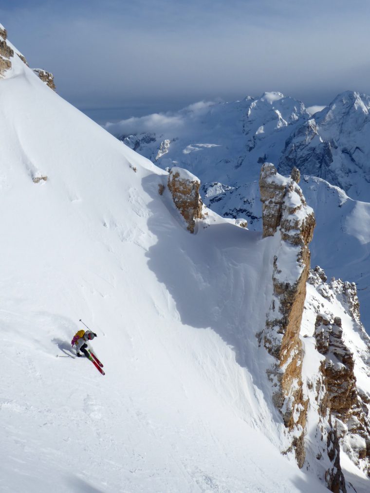 Skier with backpack skiing down steep mountain face