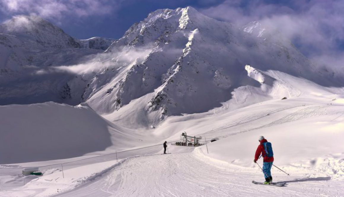 Skier in red jacket skiing down a snowy slope to a ski lift