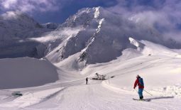 Skier in red jacket skiing down a snowy slope to a ski lift