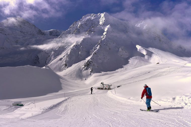 Skier in red jacket skiing down a snowy slope to a ski lift