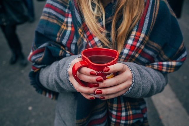 Young woman with red painted nails holding a red cup of mulled wine