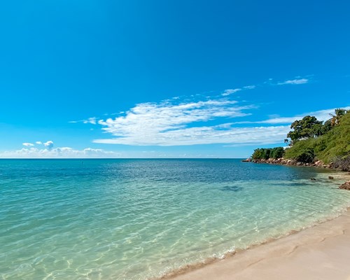 Crystal clear sea with bluey sky and beige sands with peaceful palm trees on the right