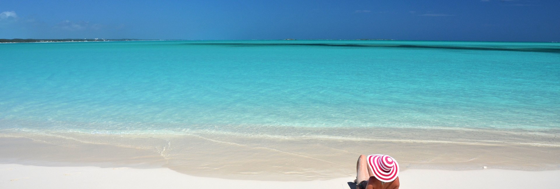 Woman with orange drink laying on white sand beach in the Bahamas