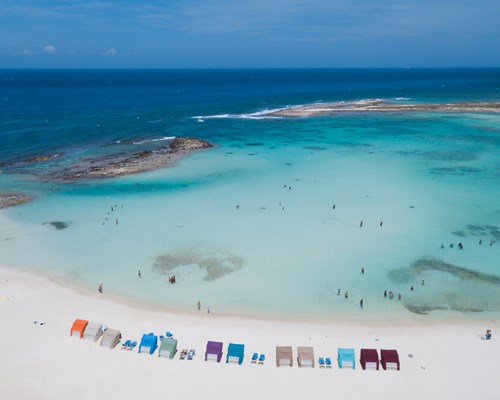 Aerial View Of Colourful Beach Huts On A White Sand Beach and people swimming in clear blue sea