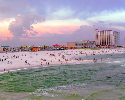 Crowds of people on Pensacola Beach fringed by a handful of resorts