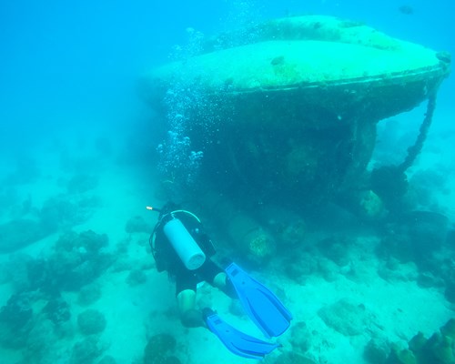 Scuba diver looking at a mini submarine wreck on the sea bed