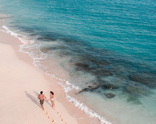 Couple walking on serene beach leaving trail of footprints behind with diamond blue ocean