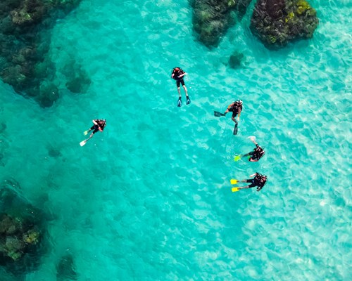 Aerial shot of a group of scuba divers near some rocks in clear bright blue sea