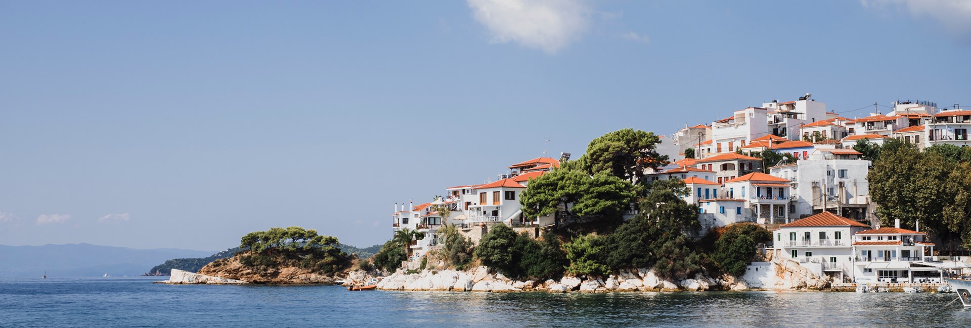 white buildings with orange roofs on Skiathos island by blue sea