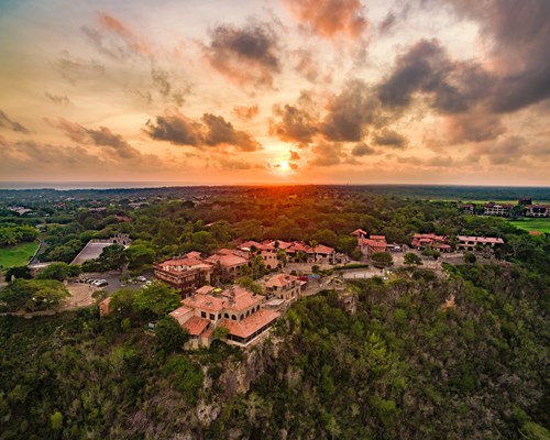Aerial view of a sun setting behind a small, old village on top of a hill