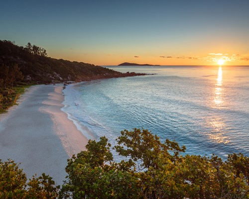 Sun setting on white shoreline with green hilly forest edging the beach - Petite Anse 