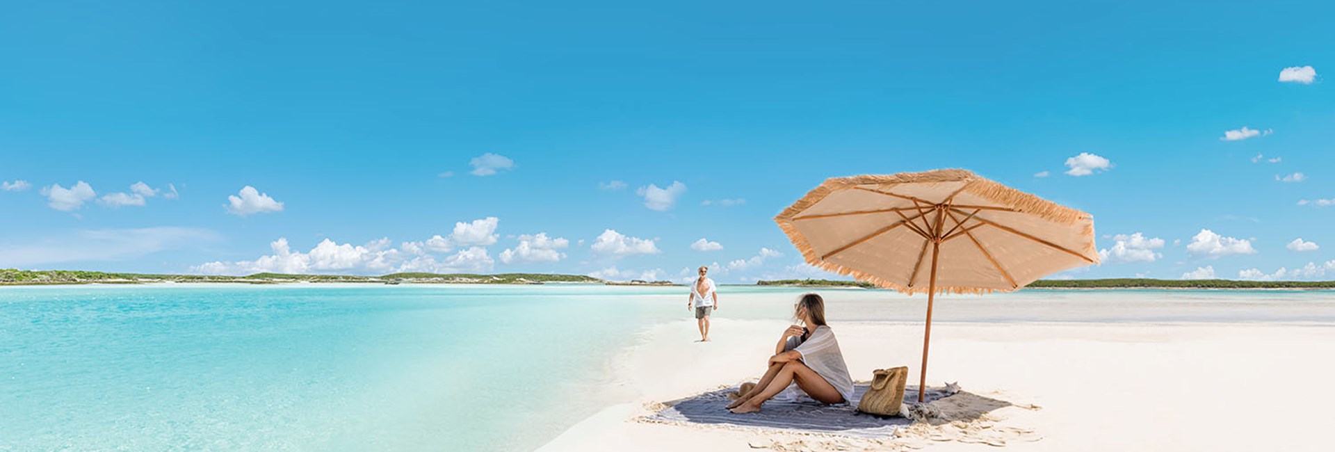 woman under parasol on sandy beach against turquoise Caribbean ocean & azure sky