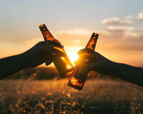 2 beer bottles knocking together with sunset shining through