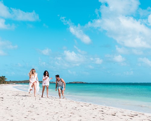 Two girls and a boy walking along a tropical white sand beach and turquoise sea