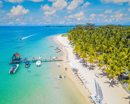 Aerial view of a beautiful white sand tropical beach with boats docked next to a small wooden dock 