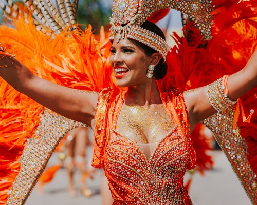 Woman in bright orange costume at a carnival on a sunny day
