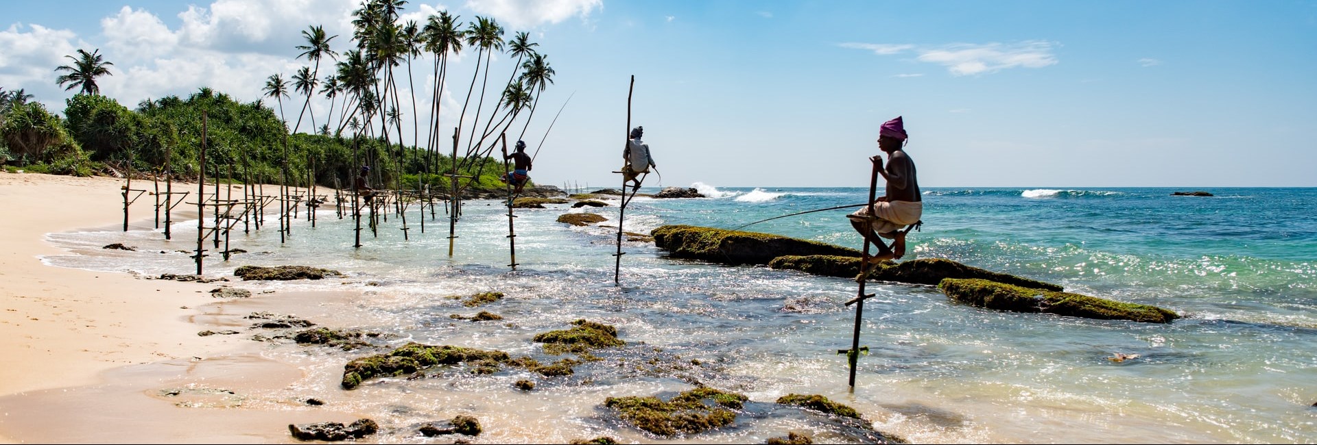 Sri Lanken men standing on sticks with a fishing pole on a wild beach