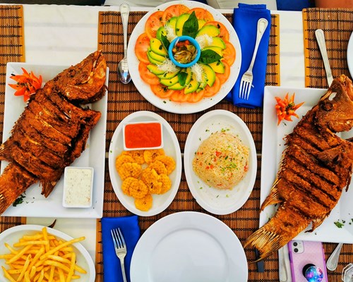 Plates of colourful food and fried fish on a wooden table