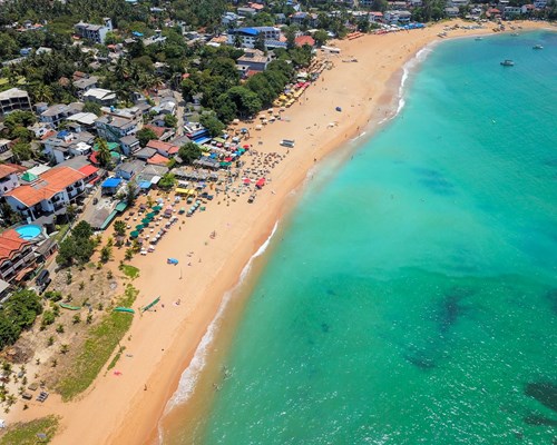 Aerial view of people near the turquoise sea on a tropical beach next to a run down village