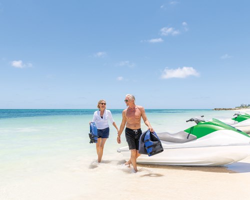Older couple walking away from jet skis on tropical beach