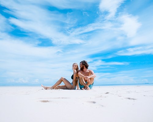 Young couple sitting on an empty white beach