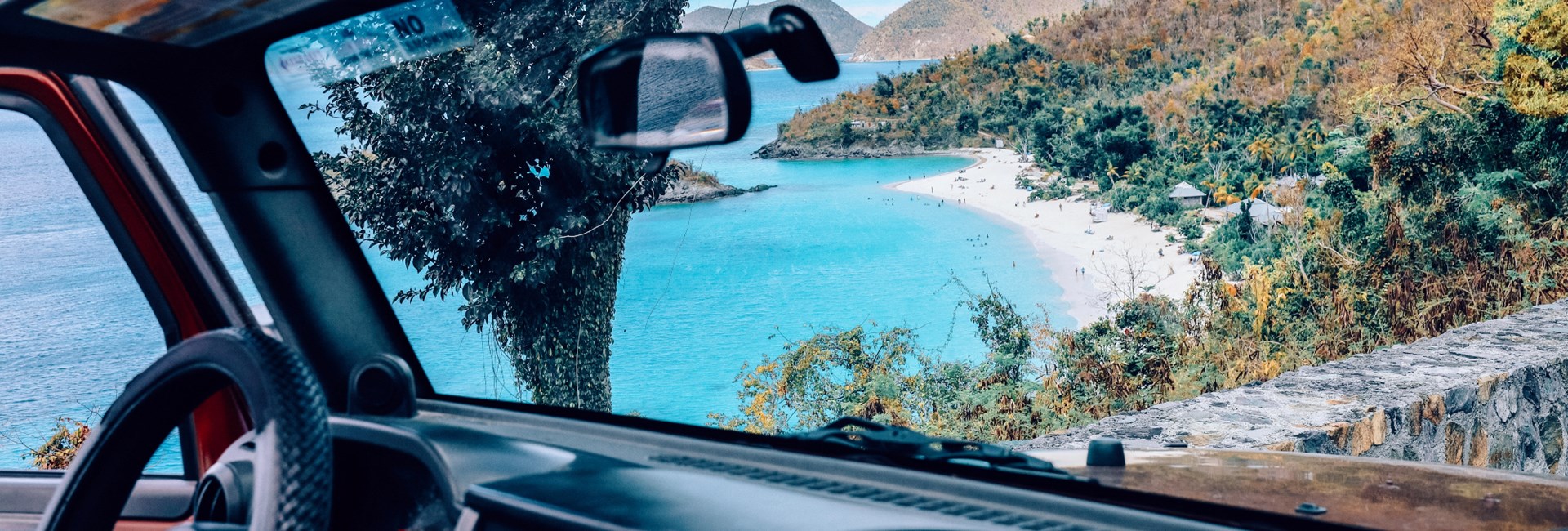 View of sandy beach and leafy mountains through car windscreen - BVI