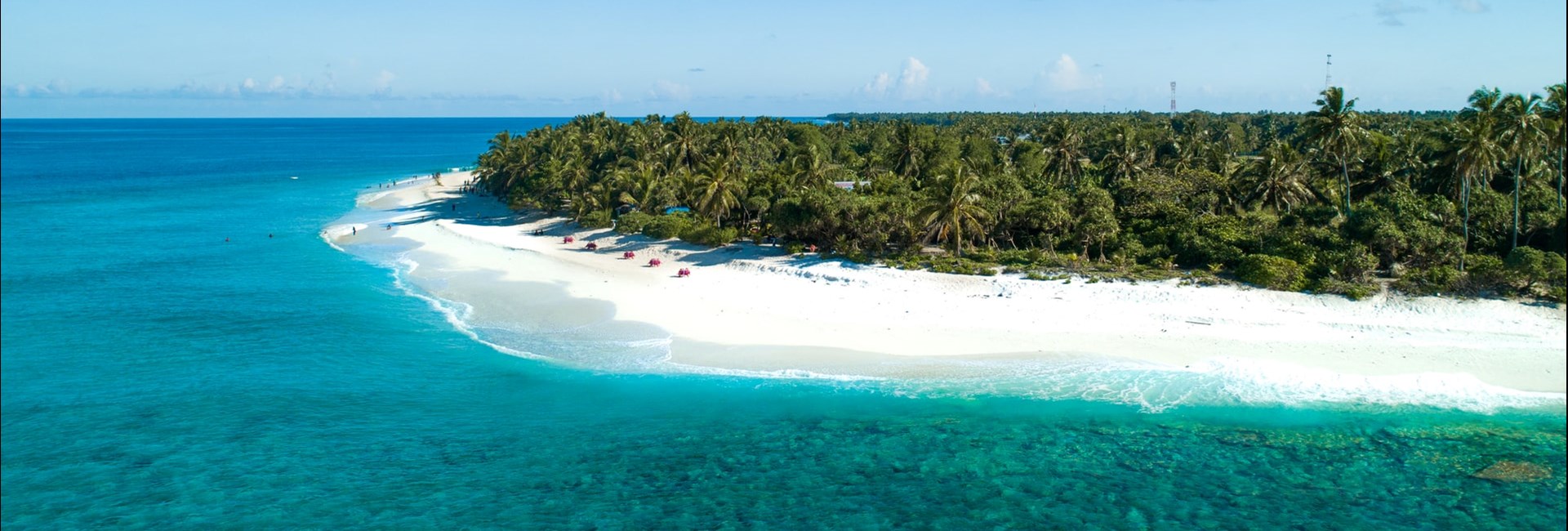 Aerial view of a bright white-sand beach island on the edge of a dense forest of palm trees