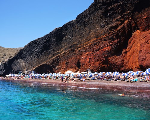 beachgoers sunbathing on Red Beach in Santorini by turquoise sea and red cliffs