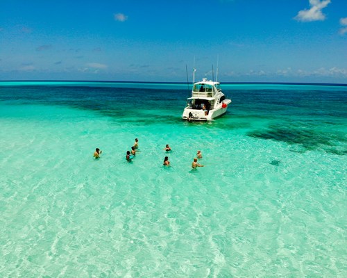People in clear green sea in the Caribbean next to docked yacht 