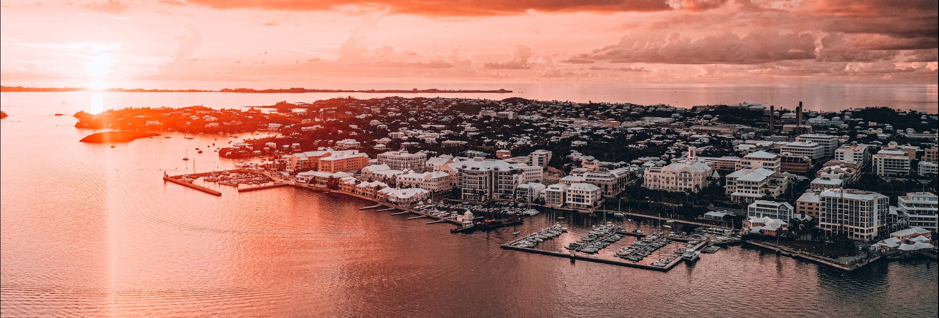 Aerial view of a red sun set in the distance above a town on the edge of an island