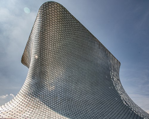  Silver tiled building shaped like a wave against a cloudy sky 