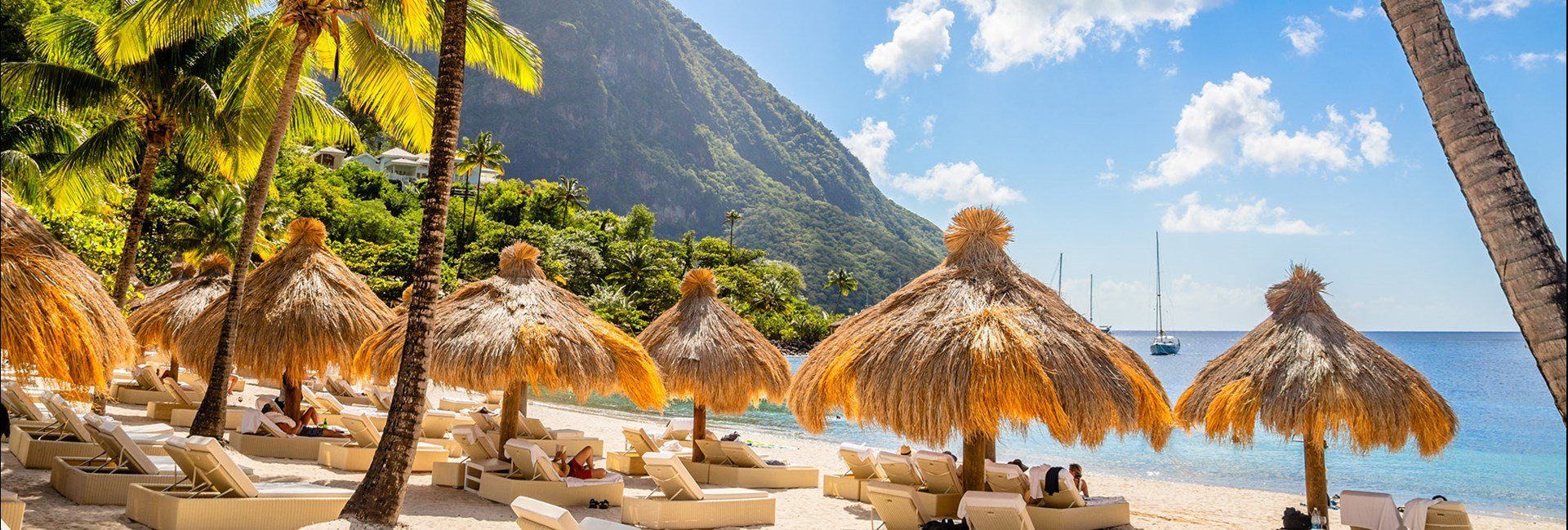 Caribbean beach with palms and straw umbrellas on the shore with Gros Piton mountain in background