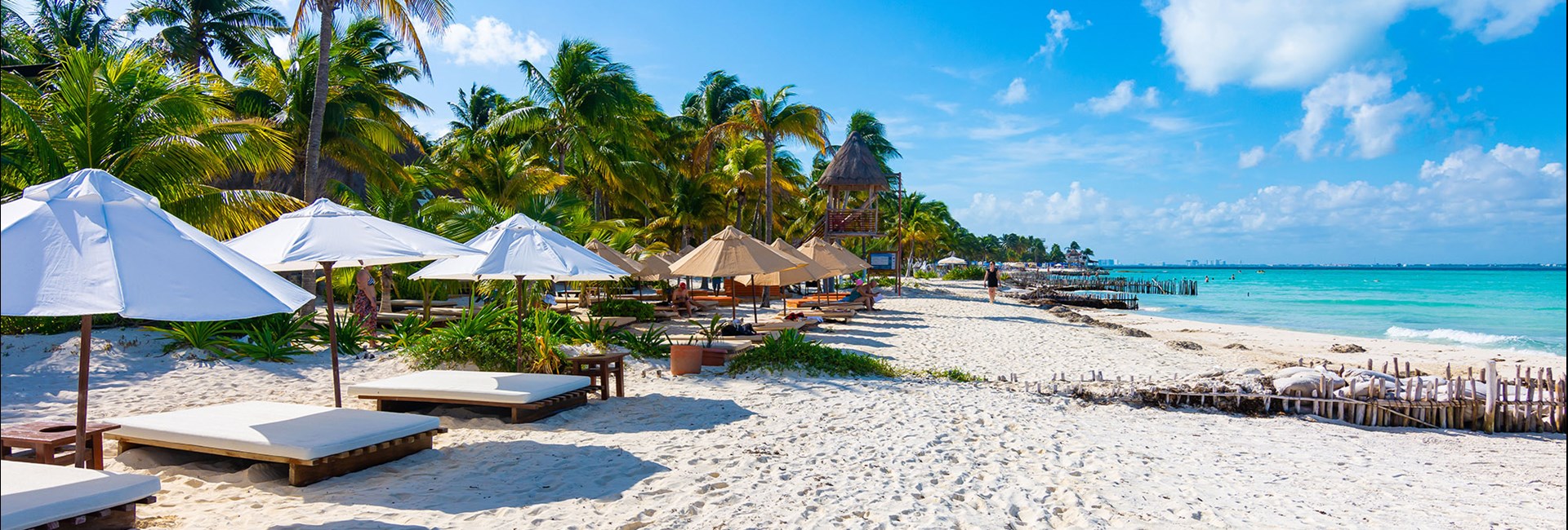 Sun beds with white umbrellas lines up along tropical white sand beach 