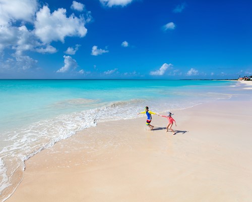 Two kids having fun at the beach running across white sand towards beautiful turquoise sea 