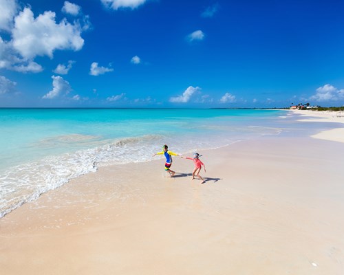 Two kids having fun at the beach running across white sand towards beautiful turquoise sea