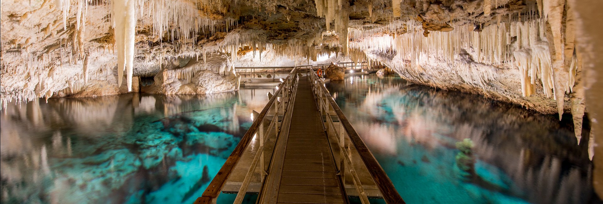 Wooden walkway over a clear pool of blue water in an underground cave