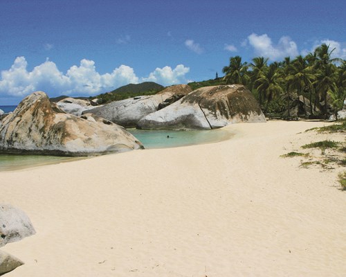 White beach with giant boulders and swaying palms with blue skies in background - Peter island, BVI