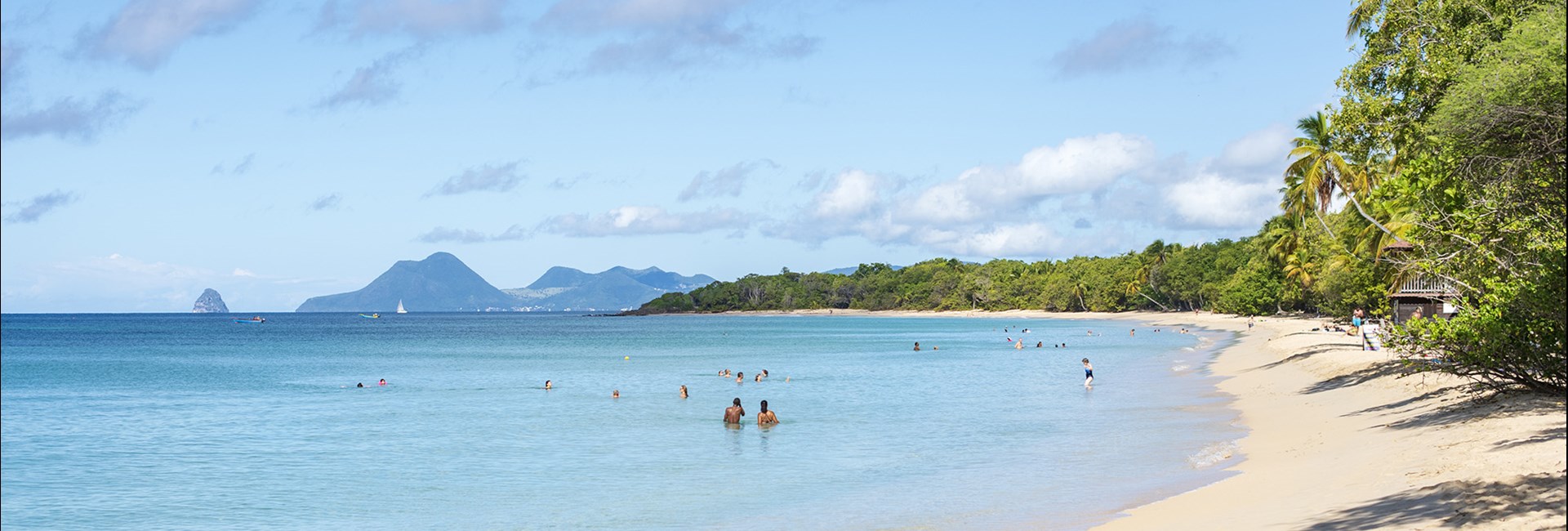 People swimming in the water at a narrow tropical beach lined with tall palm trees