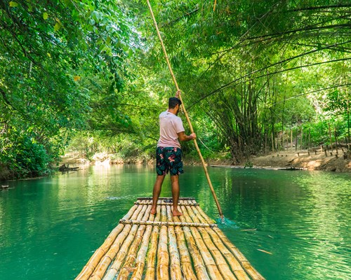 Man rowing bamboo raft along a bright green river 