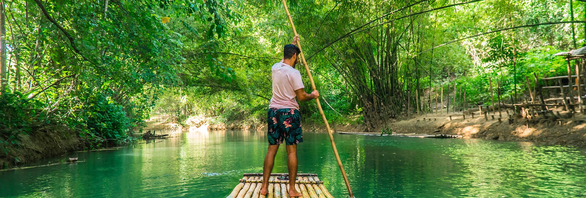 Man rowing bamboo raft along a bright green river in Jamaica